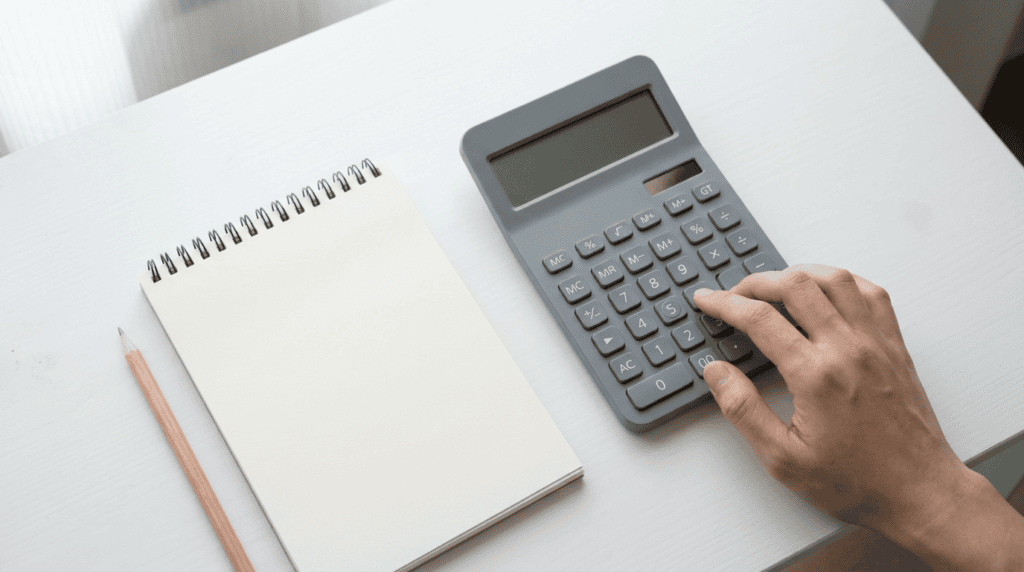 xrp price calculator - hand pressing keys on a grey desktop calculator beside a notepad