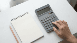 xrp price calculator - hand pressing keys on a grey desktop calculator beside a notepad
